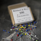 portrait image, grey slate background, pin box blurred in background, multicoloured pins scattered in focus.