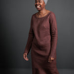 portraight image, black background. woman standing, modelling, maroon clay colour dress, knee length, long sleeve, cotton, straight dress.
