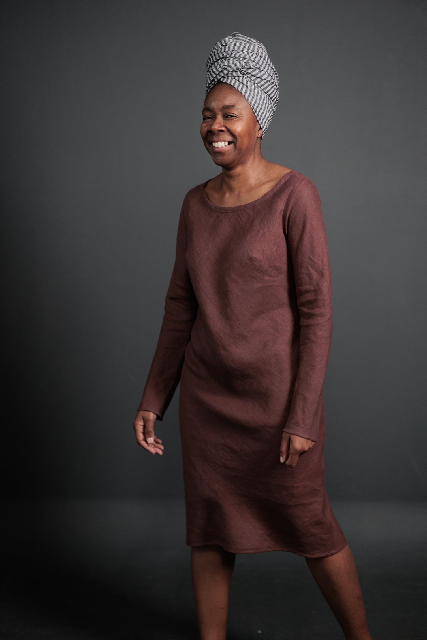 portraight image, black background. woman standing, modelling, maroon clay colour dress, knee length, long sleeve, cotton, straight dress.