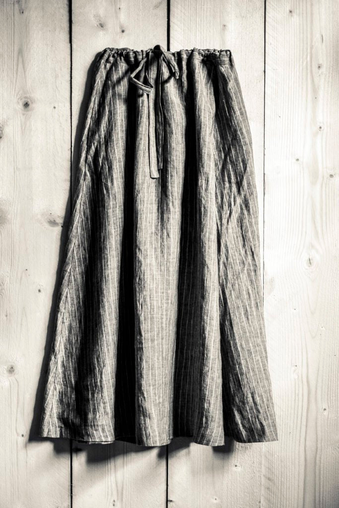 sepia toned portrait image, wooden floor board background, dark coloured grey and white stripe draw string shin length skirt.