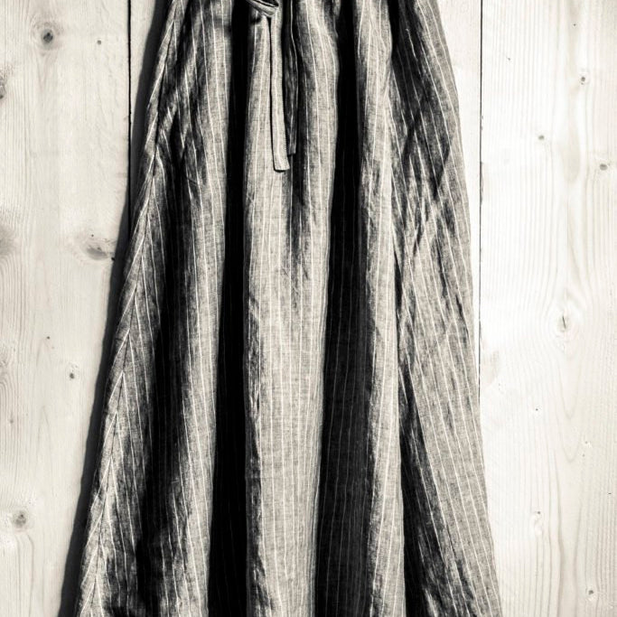 sepia toned portrait image, wooden floor board background, dark coloured grey and white stripe draw string shin length skirt.